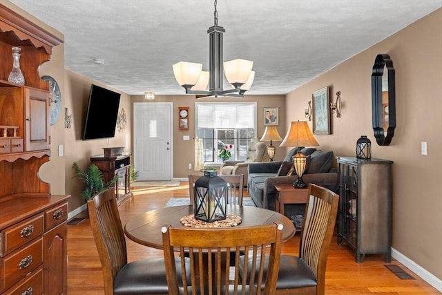 dining room featuring light wood finished floors, baseboards, visible vents, and an inviting chandelier