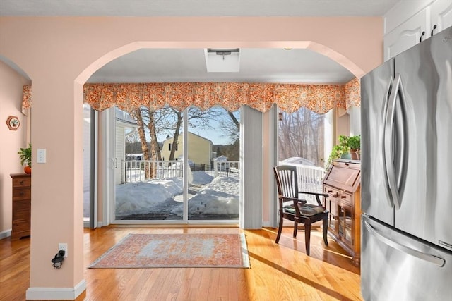 doorway featuring arched walkways, light wood-style flooring, and baseboards