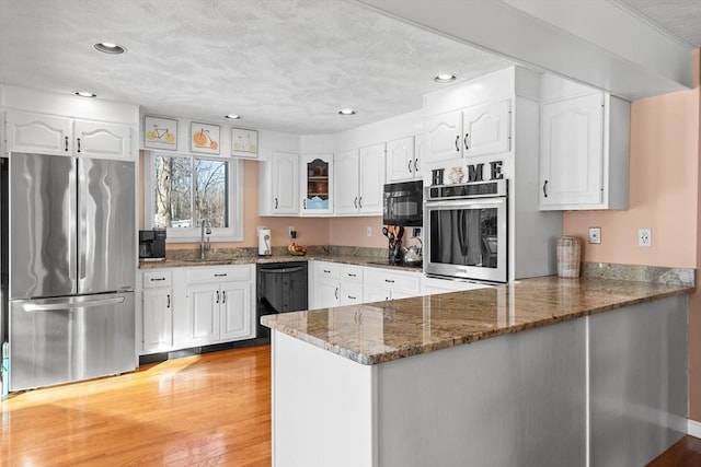 kitchen with dark stone counters, white cabinets, a peninsula, and black appliances