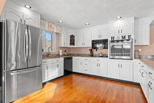 kitchen featuring black appliances, a sink, light wood-style flooring, and white cabinets