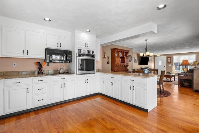 kitchen featuring decorative light fixtures, open floor plan, white cabinetry, a peninsula, and black appliances