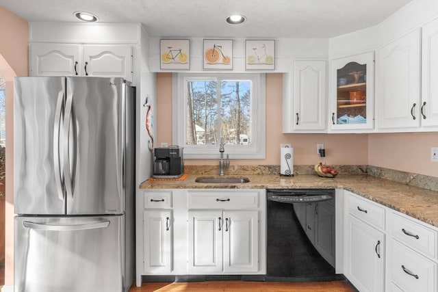 kitchen with dishwasher, a sink, freestanding refrigerator, and white cabinets