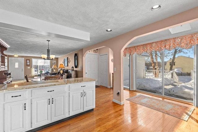 kitchen with open floor plan, arched walkways, white cabinetry, and decorative light fixtures