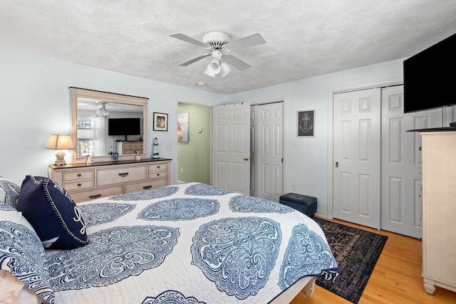 bedroom with multiple closets, ceiling fan, a textured ceiling, and light wood finished floors