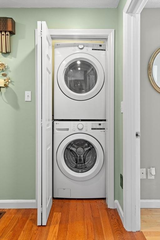 laundry room with laundry area, baseboards, light wood-style floors, and stacked washer / drying machine