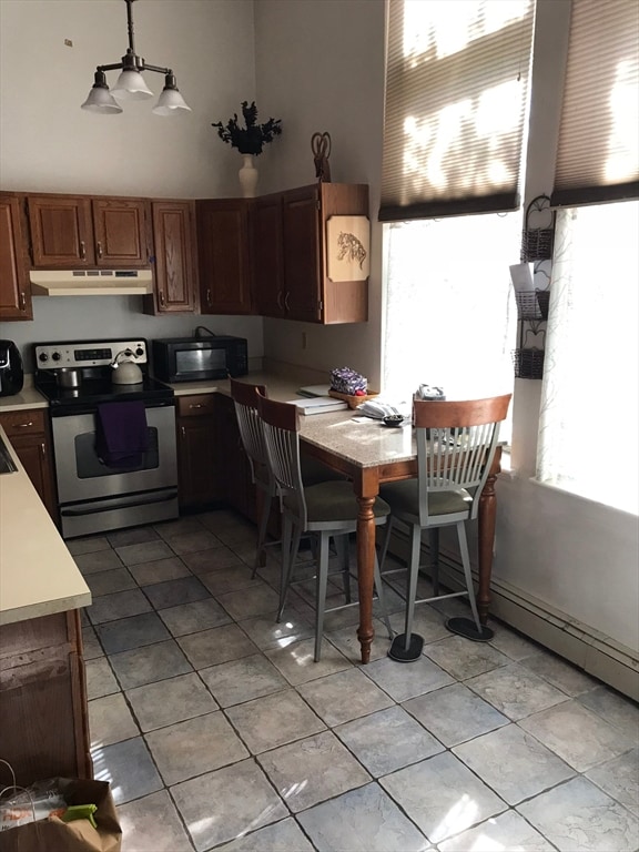 kitchen featuring stainless steel range with electric stovetop, decorative light fixtures, light tile patterned flooring, and a towering ceiling