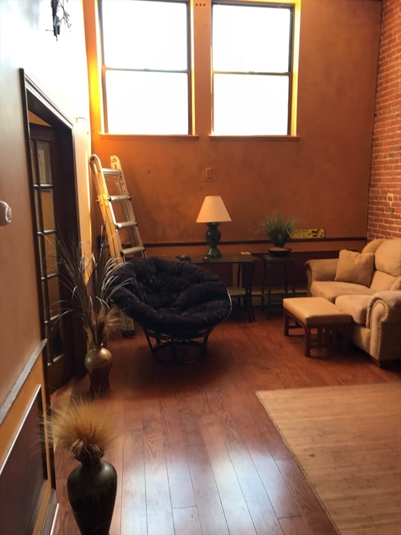 living area with hardwood / wood-style floors, a healthy amount of sunlight, and brick wall