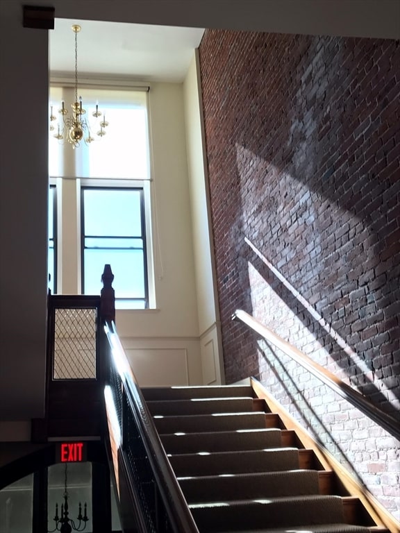 staircase with a healthy amount of sunlight, brick wall, and a chandelier