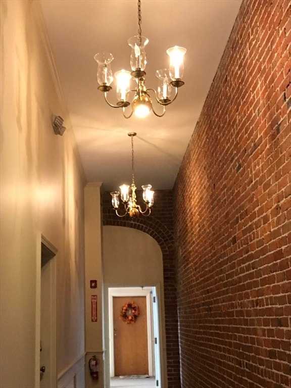 corridor featuring a notable chandelier, ornamental molding, and brick wall