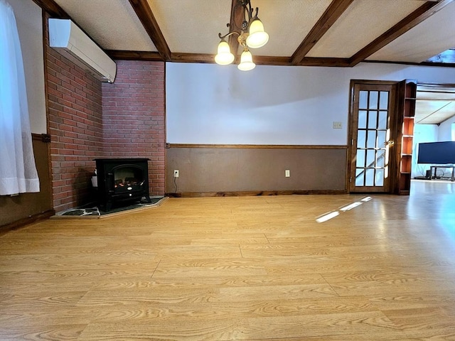 unfurnished living room featuring beam ceiling, light hardwood / wood-style flooring, a wall unit AC, and a chandelier