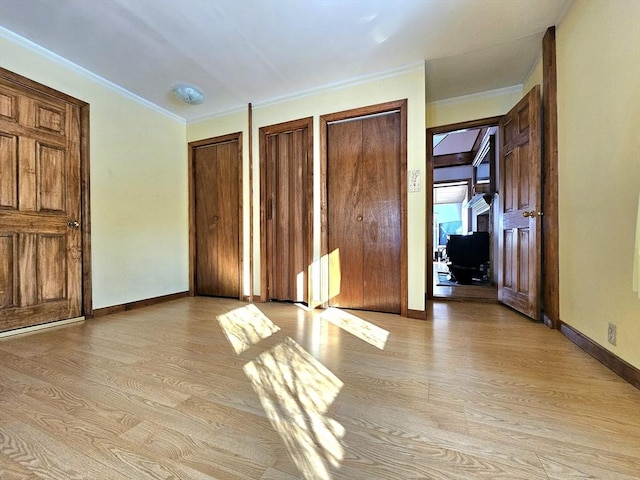 unfurnished bedroom featuring crown molding, light wood-type flooring, and two closets