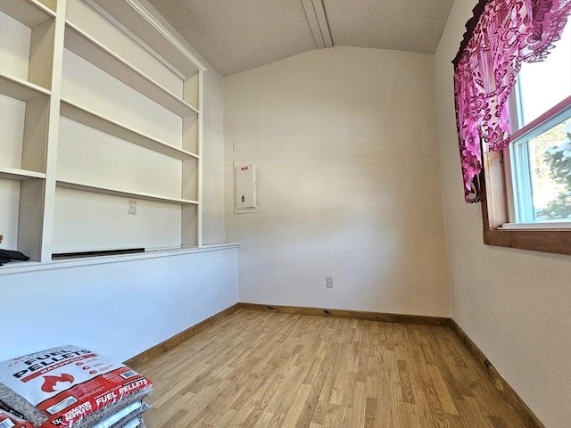 spare room featuring lofted ceiling, electric panel, and light wood-type flooring