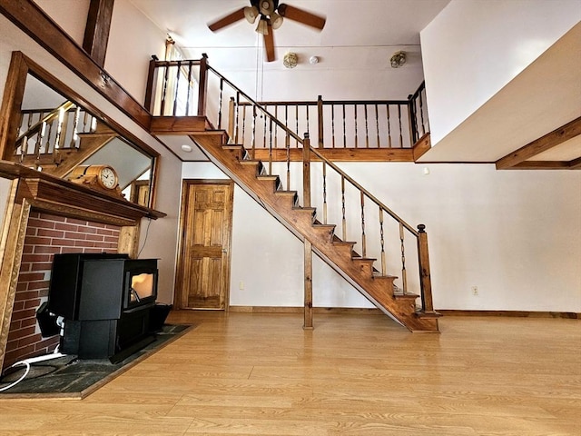 interior space featuring ceiling fan, light wood-type flooring, a high ceiling, and a wood stove