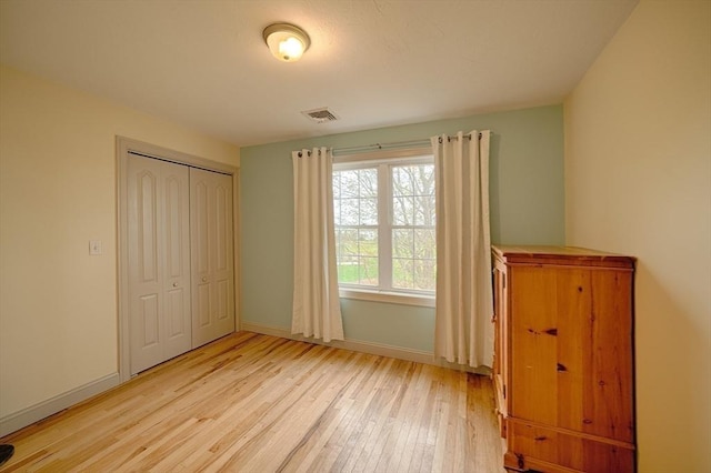 unfurnished bedroom featuring baseboards, visible vents, light wood finished floors, and a closet