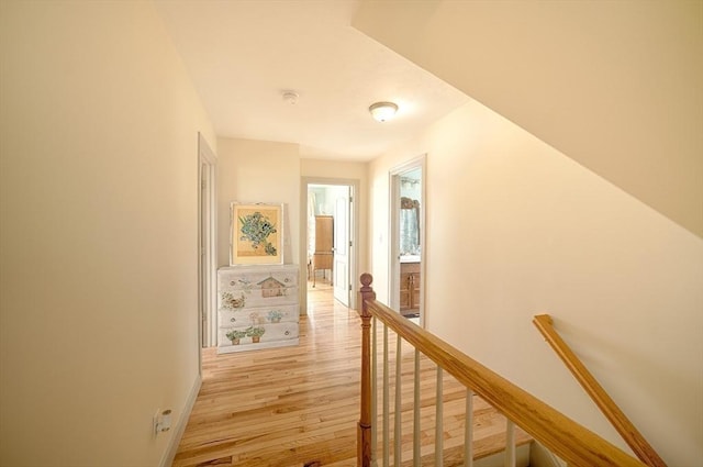 corridor with baseboards, an upstairs landing, and light wood-style floors