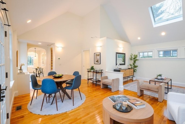 dining space with light hardwood / wood-style flooring, a skylight, and high vaulted ceiling