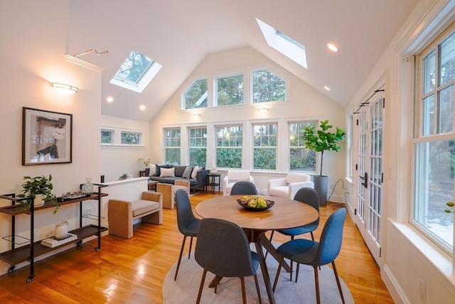 dining space with high vaulted ceiling, a skylight, and light hardwood / wood-style floors