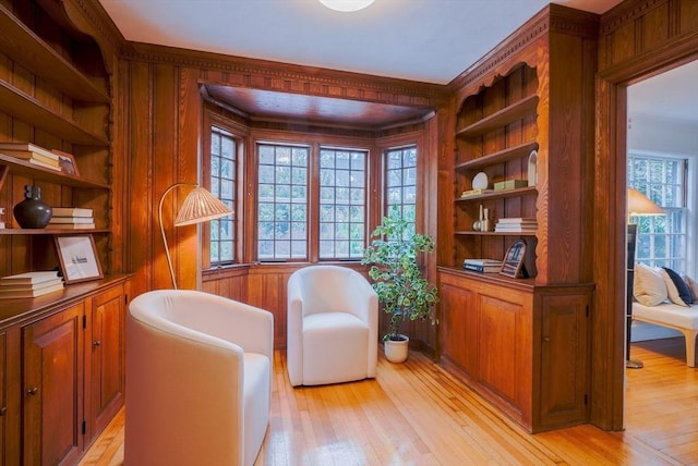 living area featuring built in shelves, light hardwood / wood-style floors, and wood walls