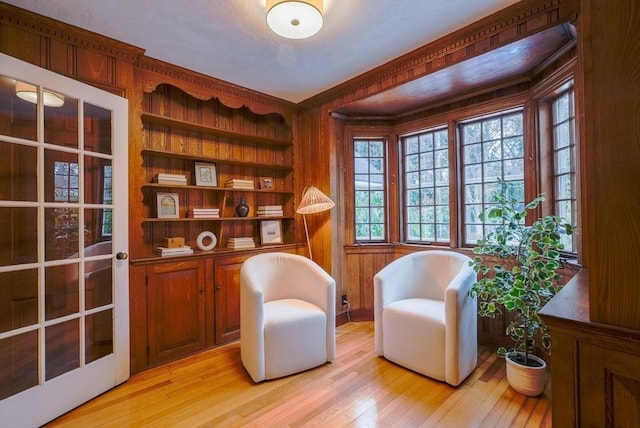 living area with ornamental molding, wooden walls, and light hardwood / wood-style flooring