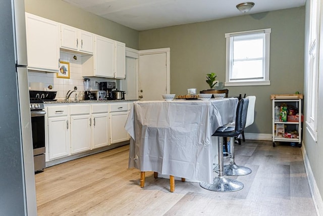 58-60 Virginia St, Springfield, MA 01108 - kitchen featuring white cabinets, light wood-type flooring, tasteful backsplash, stainless steel gas range, and a sink
