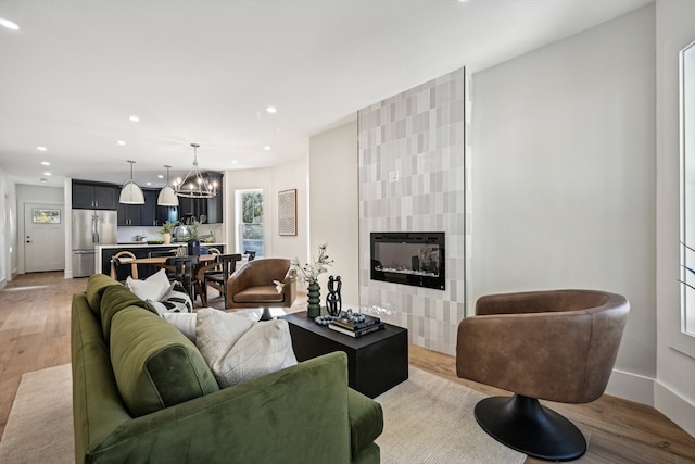 living room with light hardwood / wood-style floors, a tile fireplace, and an inviting chandelier