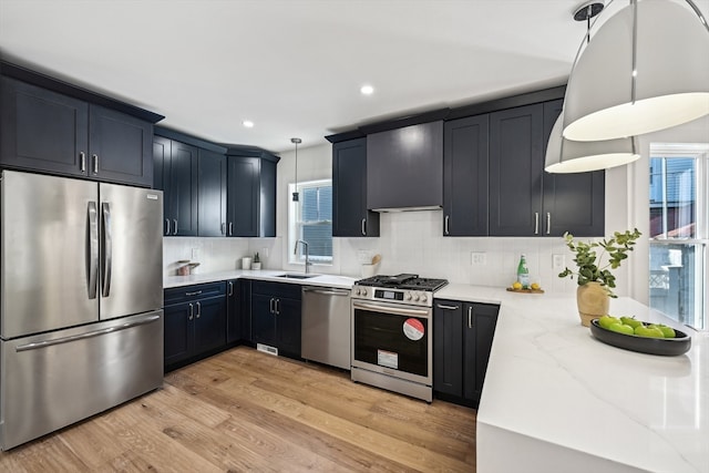 kitchen featuring stainless steel appliances, light hardwood / wood-style floors, sink, decorative light fixtures, and decorative backsplash