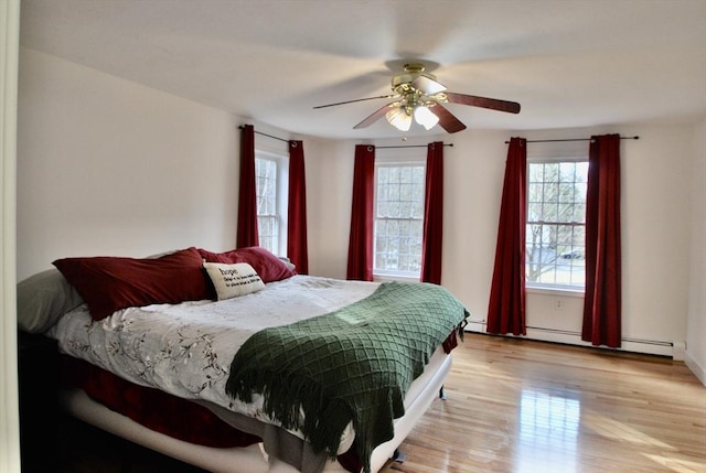 bedroom with light wood-style flooring, ceiling fan, and a baseboard radiator