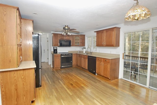 kitchen with light wood finished floors, a sink, black appliances, light countertops, and brown cabinets