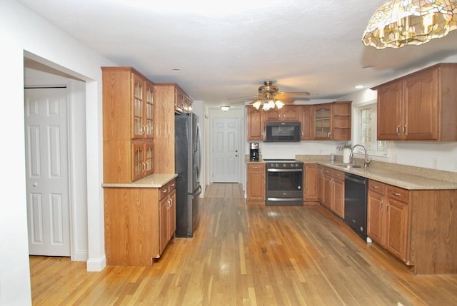 kitchen with brown cabinetry, a sink, black appliances, light countertops, and light wood-style floors