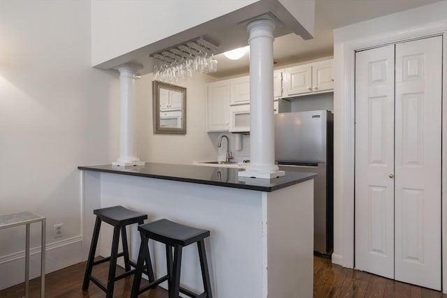 kitchen featuring white microwave, freestanding refrigerator, white cabinets, a sink, and ornate columns