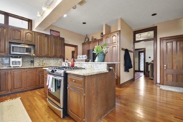 97 Livingston Ave, Lowell, MA 01851 - kitchen featuring tasteful backsplash, light wood-type flooring, appliances with stainless steel finishes, light stone countertops, and a kitchen island