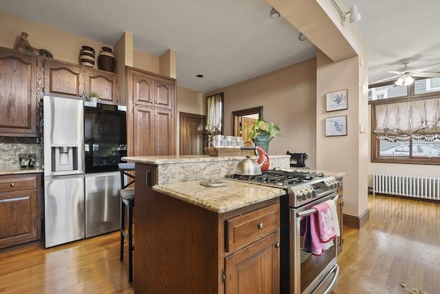 97 Livingston Ave, Lowell, MA 01851 - kitchen featuring radiator, light wood-type flooring, a ceiling fan, a kitchen island, and stainless steel appliances