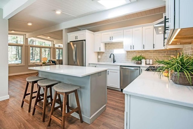 kitchen featuring stainless steel appliances, lofted ceiling with beams, white cabinetry, a kitchen island, and a kitchen breakfast bar