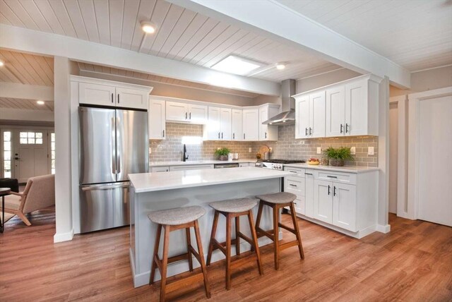 kitchen with appliances with stainless steel finishes, light countertops, white cabinets, and wall chimney exhaust hood