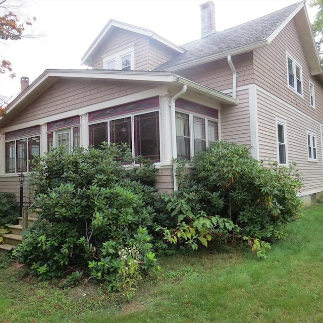 view of home's exterior with a shingled roof, a sunroom, and a chimney