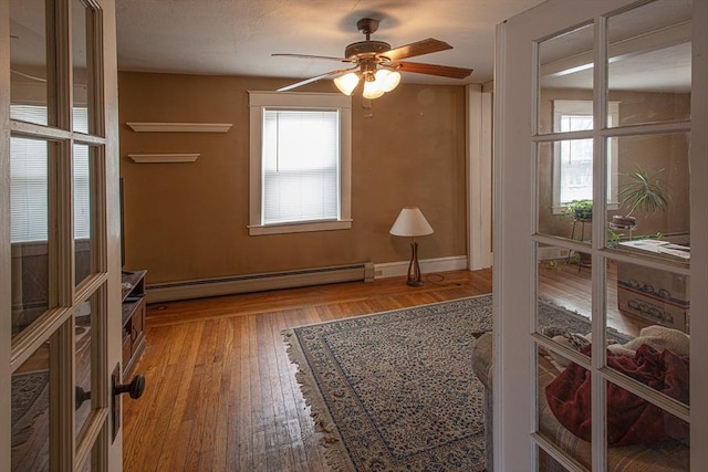 empty room with a baseboard heating unit, wood-type flooring, ceiling fan, and baseboards