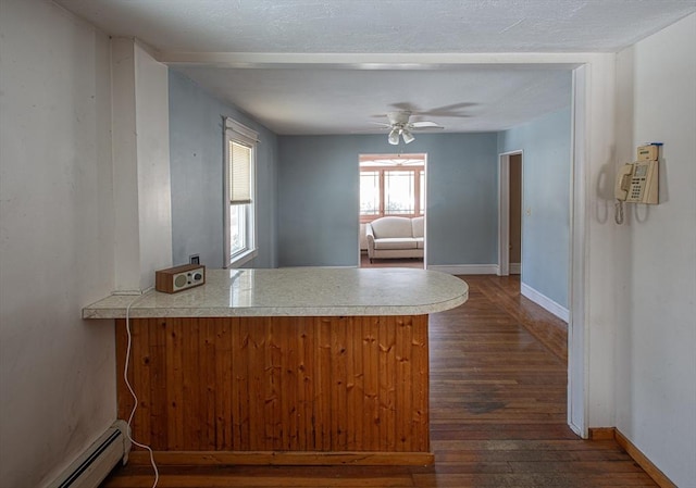 kitchen featuring a peninsula, a ceiling fan, baseboards, baseboard heating, and dark wood-style floors