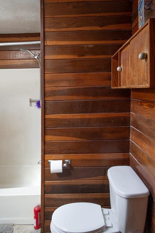 full bathroom featuring  shower combination, wood walls, and toilet