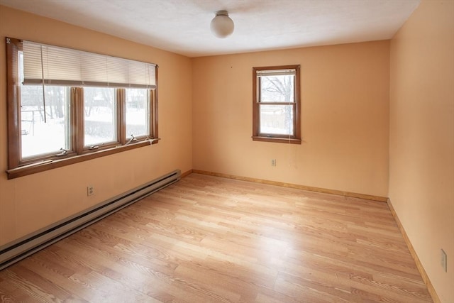 unfurnished room featuring baseboards, light wood finished floors, baseboard heating, and a healthy amount of sunlight