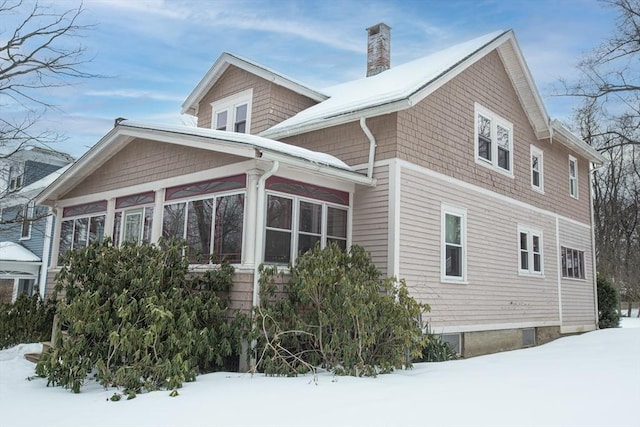 snow covered property featuring a chimney and a sunroom