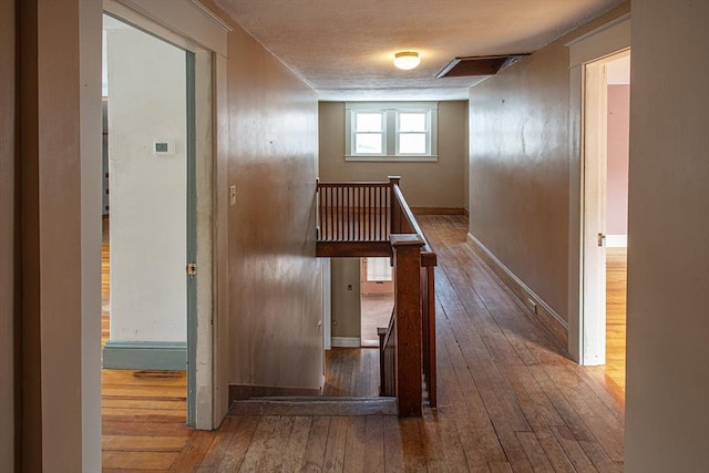 hallway featuring baseboards, hardwood / wood-style flooring, an upstairs landing, and attic access