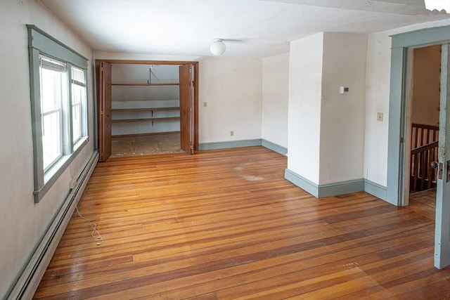 empty room featuring a baseboard radiator, baseboards, and light wood finished floors