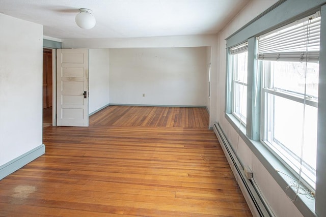 empty room with a baseboard heating unit, light wood-style flooring, and baseboards