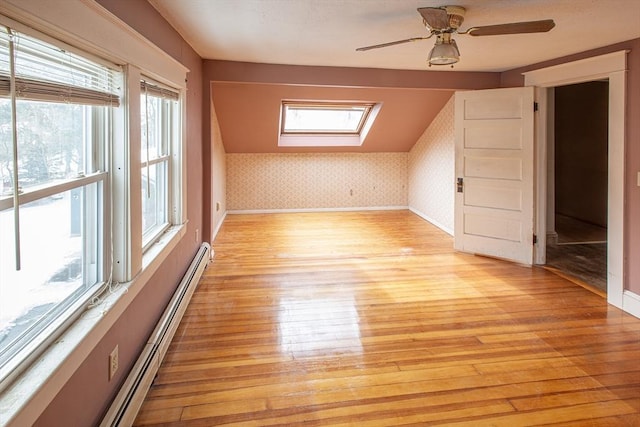 additional living space with a skylight, a baseboard heating unit, light wood-type flooring, baseboards, and wallpapered walls