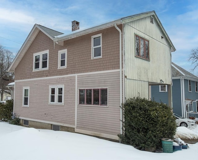 snow covered back of property featuring a chimney