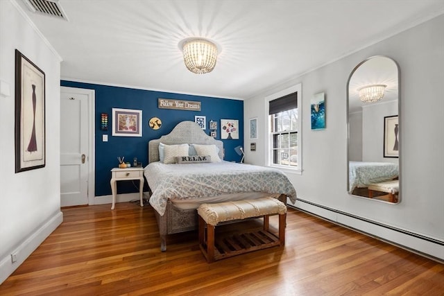 bedroom with a baseboard heating unit, an inviting chandelier, wood finished floors, and visible vents