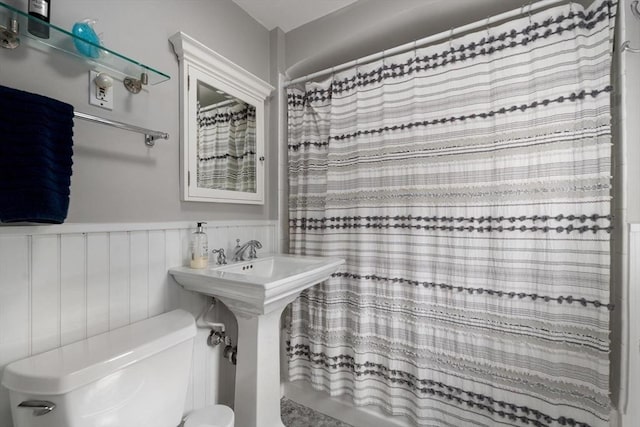 full bath featuring a wainscoted wall, curtained shower, toilet, and a sink