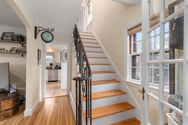 stairs featuring a healthy amount of sunlight, baseboards, ornamental molding, and wood finished floors