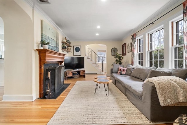 living area with light wood-style flooring, ornamental molding, arched walkways, baseboards, and stairs