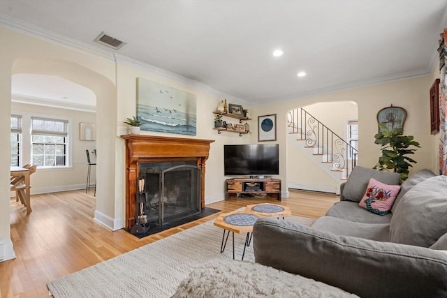 living area featuring light wood-type flooring, visible vents, arched walkways, and stairs